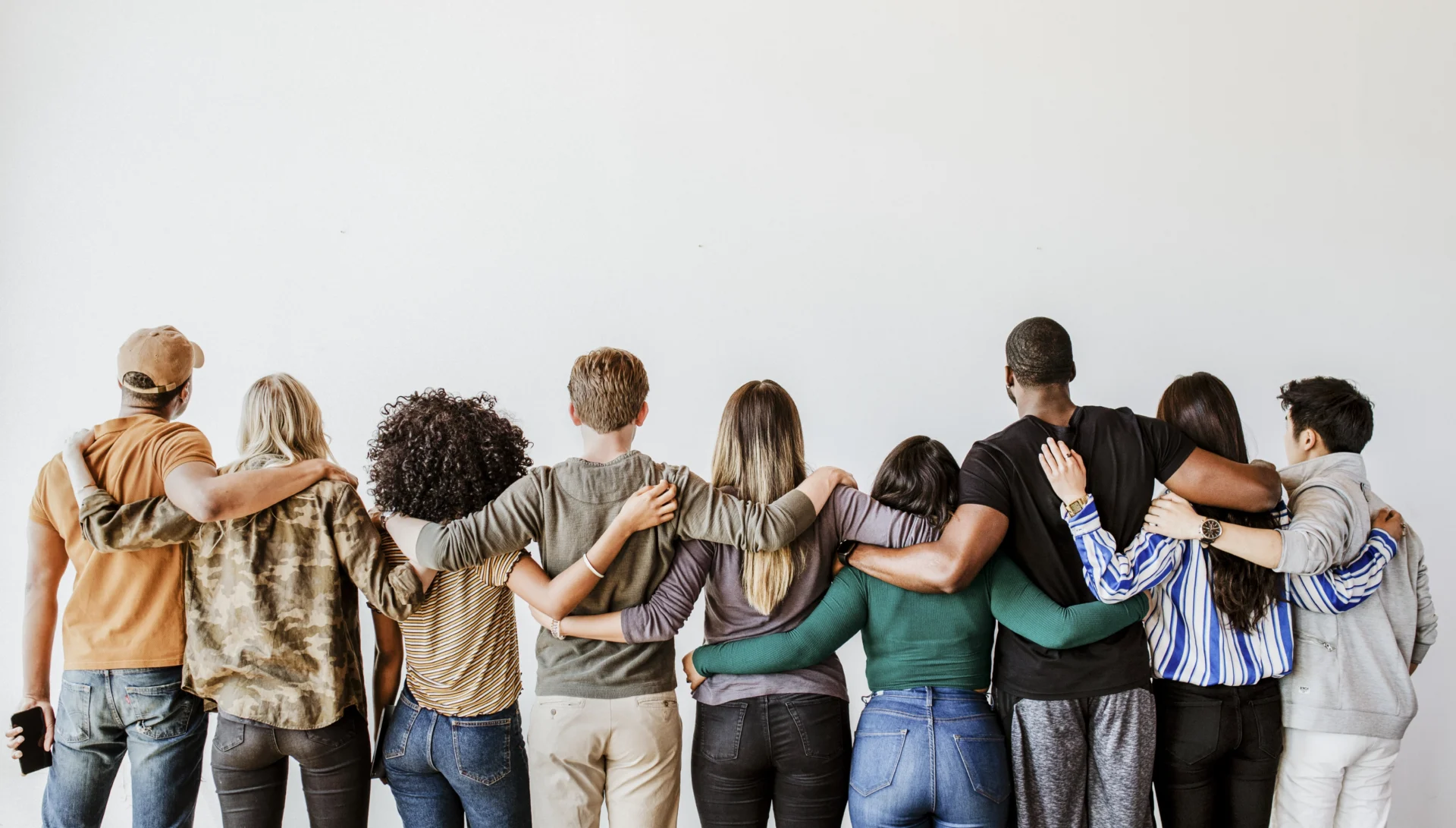Group of diverse people standing arm-in-arm facing away.