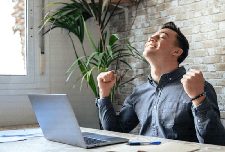Man celebrating success while working on a laptop indoors.